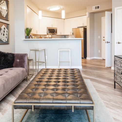 Apartments for Rent in Sparks, NV - Waterfront at the Marina - Cozy Living Room with Open-Concept Layout, View of the Kitchen, a Sofa, Cushioned Bench Seat/Coffee Table, Wood-Style Flooring, a Mounted TV, and White Walls
